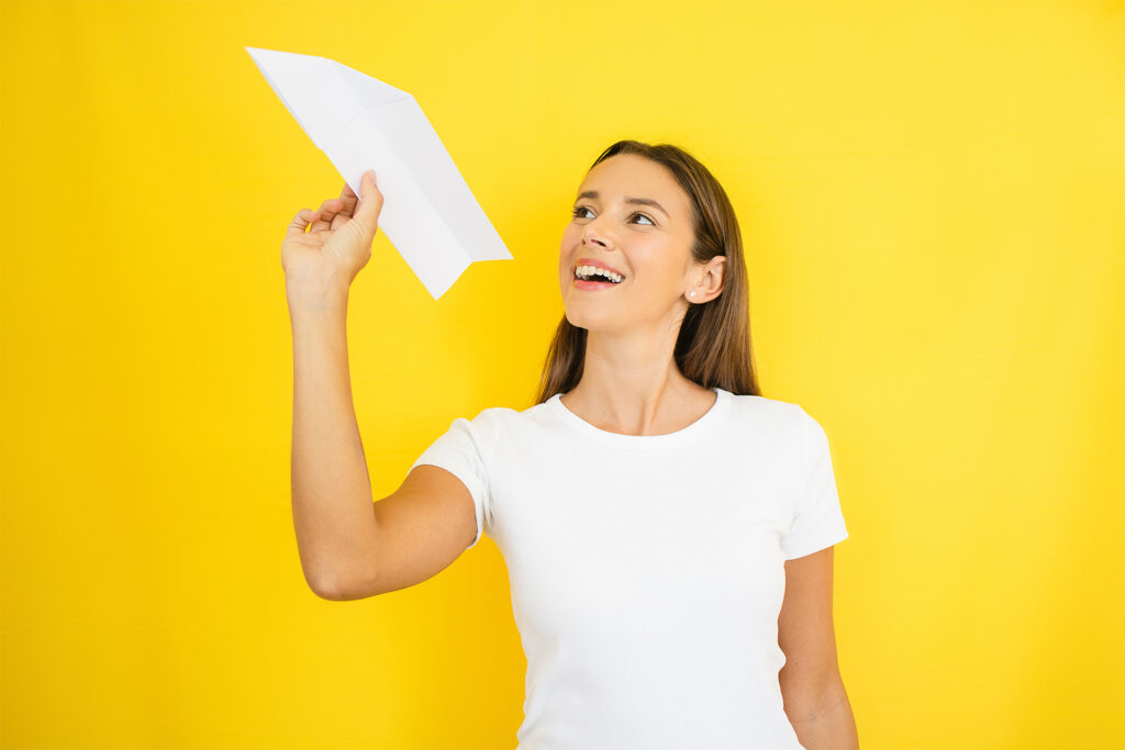 a smiley young woman poised to throw a paper aeroplane into the air