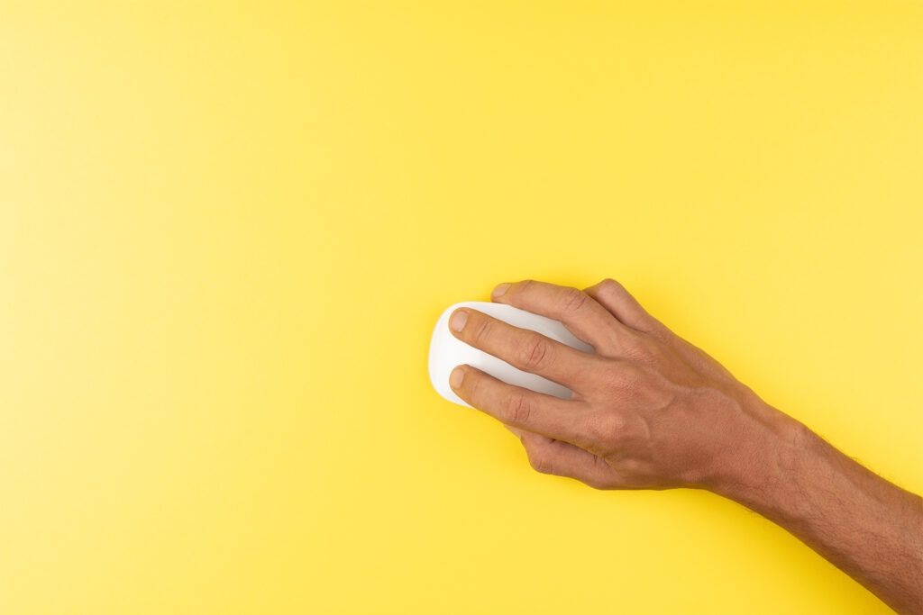 a hand holding a white wireless computer mouse on a yellow background