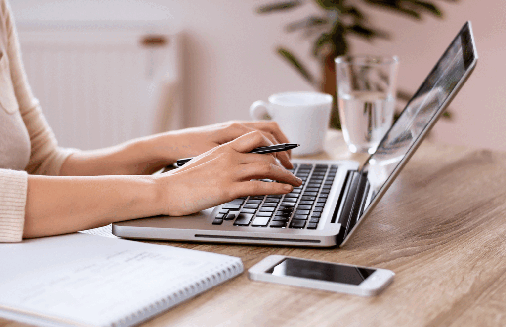 A person on a laptop with a notebook and pen writing content for ecommerce advertising.