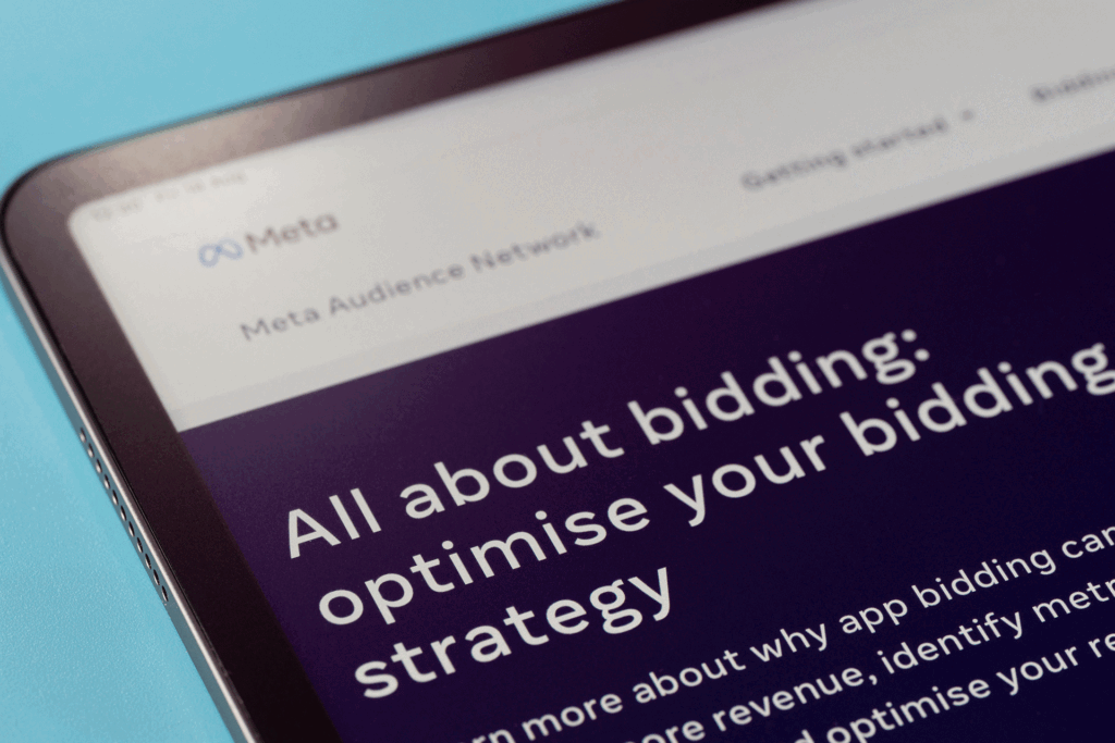 A close-up of a tablet screen on the Meta website. Text reads 'all about bidding: optimise your bidding strategy.'