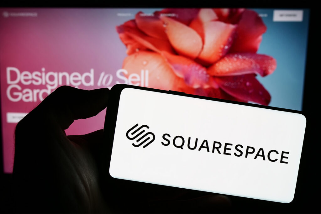 Person holding smartphone with logo of-Squarespace on screen in front of webpage