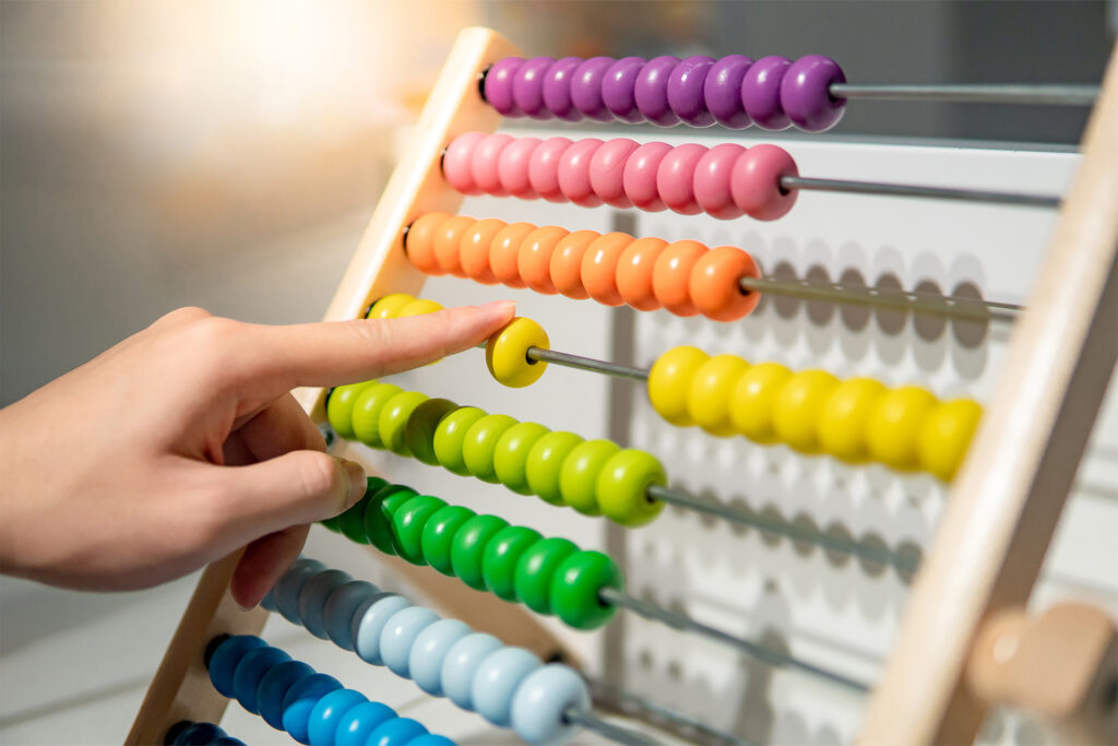 a close up of a hand pushing across yellow beads on a rainbow abacus