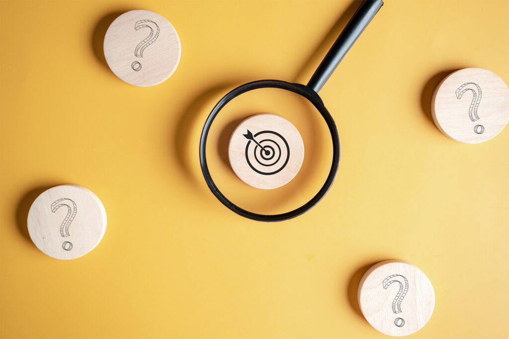 Magnifying glass hovering over a target symbol on a yellow background covered in question marks